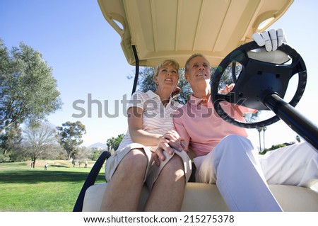 Mature couple sitting in golf buggy on golf course, man driving, smiling, front view, low angle view