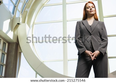 Confident businesswoman, with ginger hair, wearing grey suit, standing beside window, portrait, low angle view