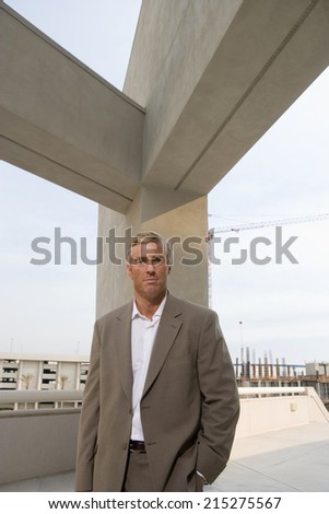 Mature businessman standing on elevated urban walkway below concrete beams, front view, portrait
