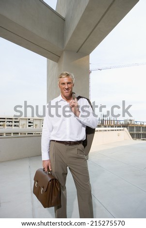 Mature businessman, with briefcase, standing on elevated urban walkway below concrete beams, front view, portrait