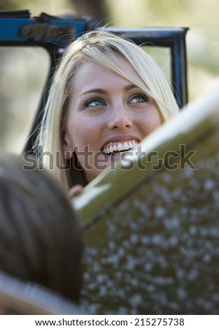 Teenage girl sitting in car with surfboard, smiling (differential focus)