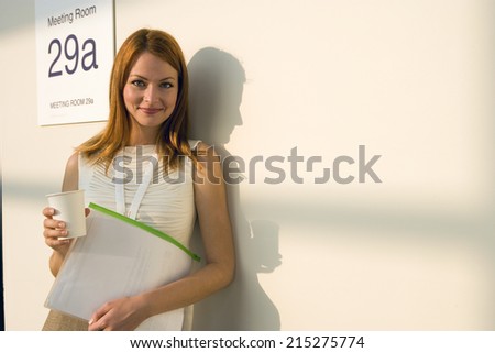 Businesswoman standing outside meeting room, taking coffee break, casting shadow on wall, smiling, portrait