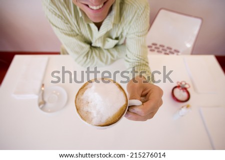 Man sitting at cafÃ?Â?Ã?Â© table, drinking cappuccino, smiling, front view, elevated view (wide angle)