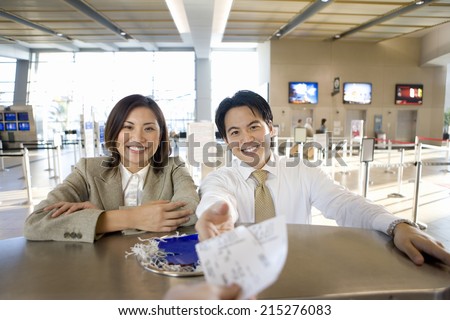 Business couple checking in at airport, businessman receiving boarding passes from check-in attendant, view from behind check-in desk (differential focus)