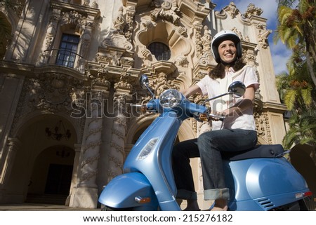 USA, California, San Diego, Balboa Park, woman riding on blue motor scooter, smiling, side view, low angle view