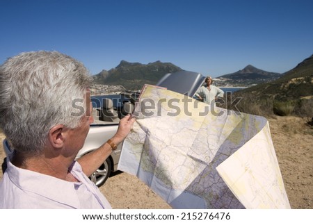 South Africa, Cape Town, mature man looking at map, woman by car in background