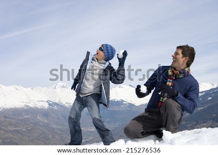 Father and son having snow ball fight in snow field, mountain range in background