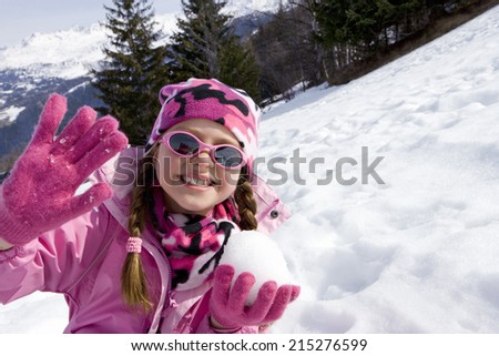 Girl wearing woolen hat and sunglasses in snow field, holding snow ball, smiling, portrait