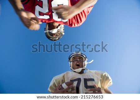 American football player running with ball at opposing player during competitive game, upward view