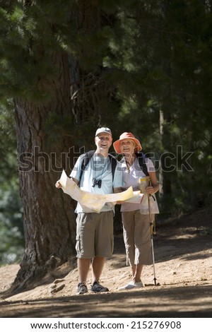 Senior couple hiking on woodland trail, man holding map, woman using hiking pole, smiling, front view