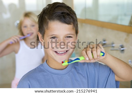 Boy and girl (6-8) brushing their teeth in bathroom, smiling, portrait