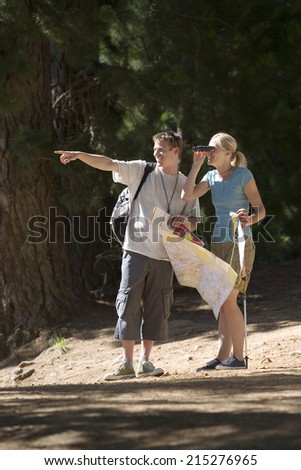 Couple hiking on woodland trail, man with map pointing, woman looking through binoculars, smiling