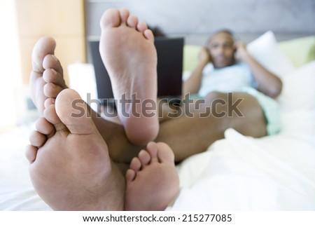 Young couple sitting on bed with laptop, feet in foreground