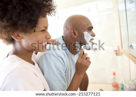 Young woman smiling at young man shaving, side view