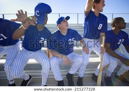 Excited baseball team jumping up from bench in stand during competitive baseball game, cheering, front view (backlit)