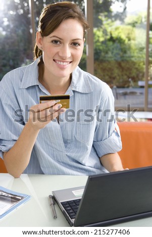 Woman holding credit card by laptop, smiling, portrait
