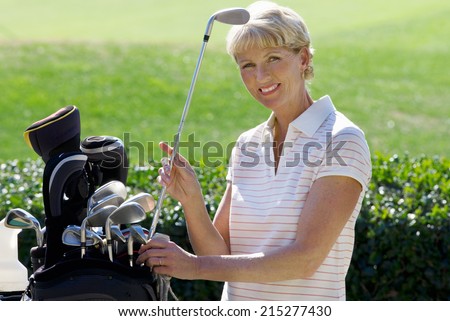 Mature woman playing golf, taking golf club from bag, smiling, side view, portrait