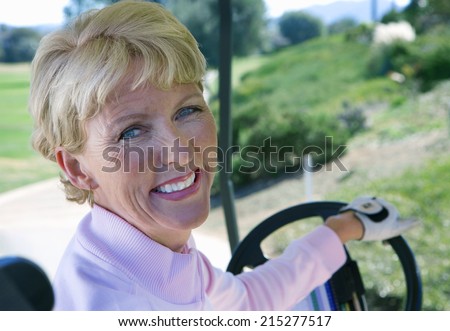 Mature woman driving golf buggy on golf course, looking over shoulder, smiling, close-up, rear view, portrait