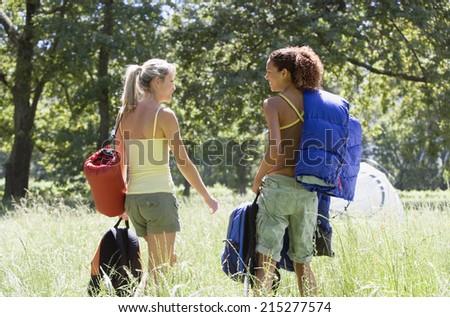 Two young women, with rucksacks and sleeping bags, departing on hiking trip in woodland clearing, rear view