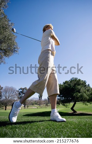Mature woman teeing off with driver on golf course, side view (surface level)