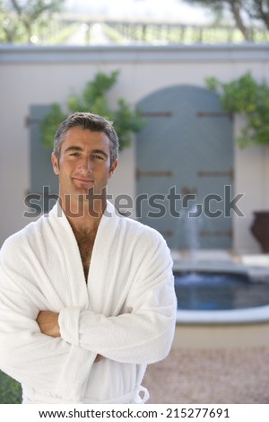 Mature man wearing white bath robe, arms crossed, smiling, portrait, fountain in background