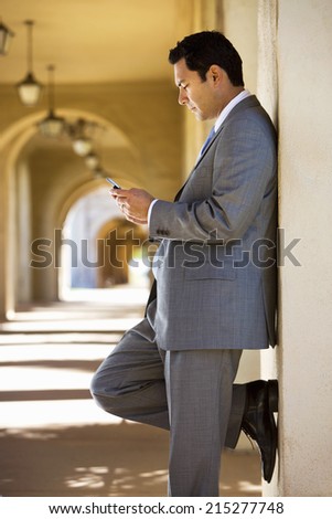 Businessman standing in building arcade, looking at text message on mobile phone, profile
