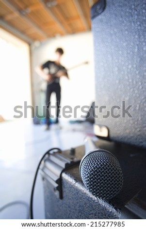Teenage boy (16-18) playing electric guitar in garage, focus on microphone in foreground