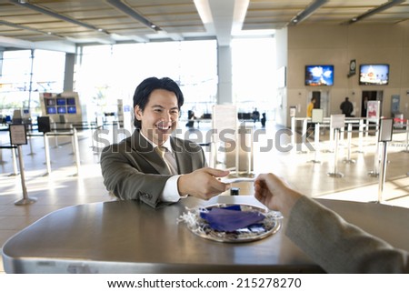 Businessman checking in at airport, receiving boarding pass from check-in attendant, view from behind check-in desk