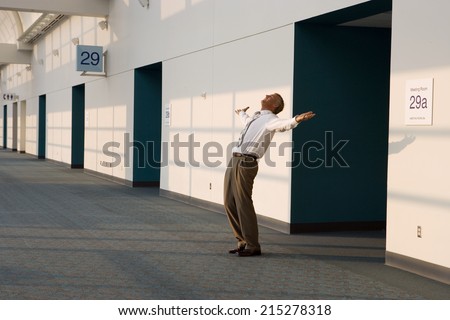 Joyous businessman standing outside meeting room, arms out and head back, smiling, side view