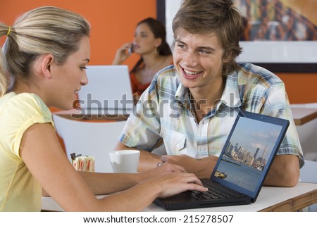 Young man smiling by young woman using laptop in cafe, young woman with laptop in background