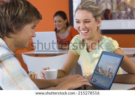Young woman laughing by young man using laptop in cafe, young woman using laptop in background