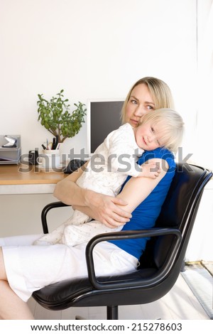 Mother embracing baby girl (21-24 months) in chair by desk in home office