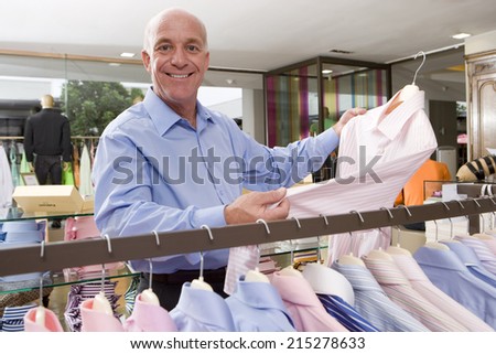 Mature man in clothing store, holding up shirt, smiling, portrait