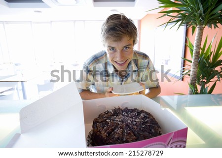 Teenage boy (16-18) smiling by chocolate cake in box, portrait