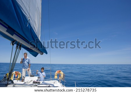 Father and son (8-10) standing at helm of sailing boat out to sea, boy steering, smiling