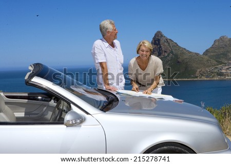South Africa, Cape Town, senior couple standing by car with map, smiling, sea in background