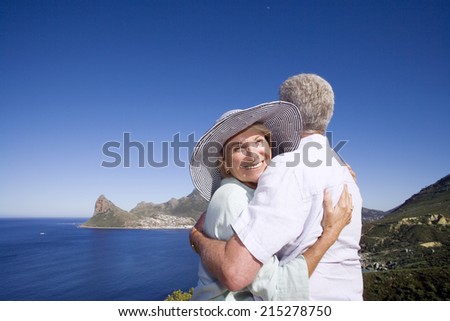South Africa, Cape Town, senior couple embracing by sea, smiling, portrait of woman