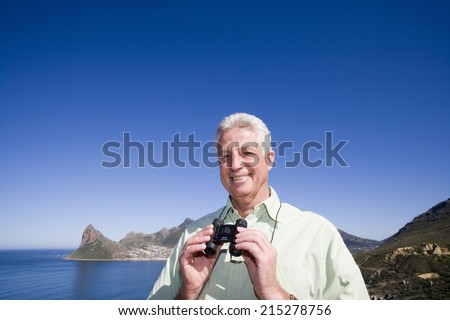 South Africa, Cape Town, senior man holding binoculars by sea, smiling, portrait