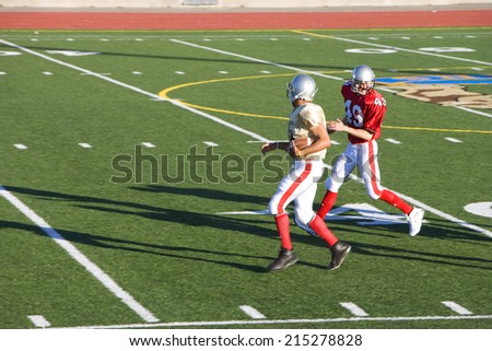 American football player chasing opposing receiver with ball during competitive game, side view
