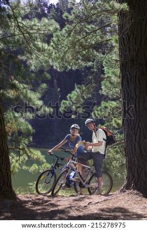 Young couple, with rucksacks, mountain biking along woodland trail beside lake, holding map, smiling, portrait