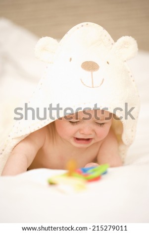 Baby girl (9-12 months) crying on bed, looking at dummy, close-up