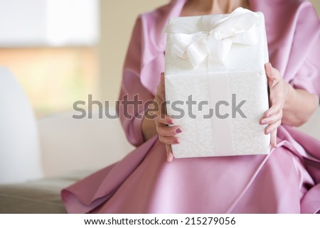 Senior woman, in pink dress, holding wedding gift, front view, mid-section