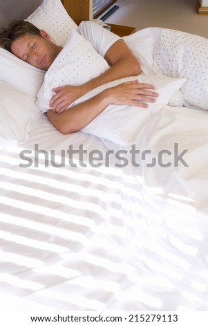 Man asleep in bed, hugging pillow, elevated view