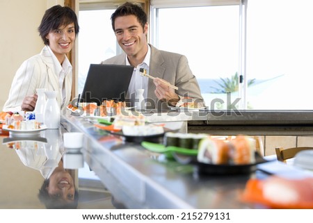 Couple with laptop in sushi bar, smiling, portrait