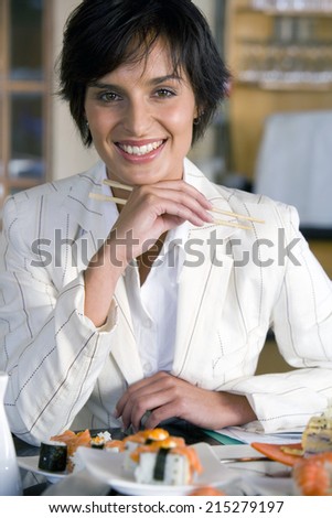 Young woman eating sushi with chopsticks, smiling, portrait