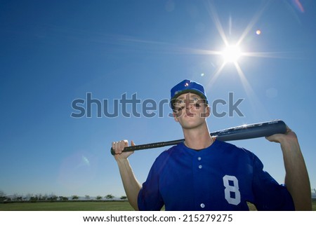 Baseball player, in blue uniform and cap, standing on pitch with bat behind head, front view, portrait (lens flare)