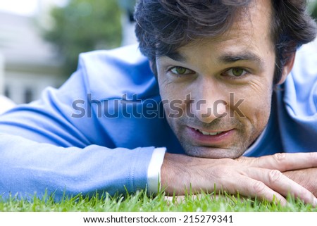 Man lying on stomach on grass resting chin in hands, smiling, portrait, close-up