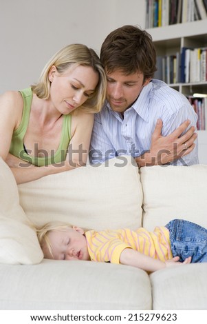 Man and woman looking at daughter (12-15 months) asleep on sofa, close-up