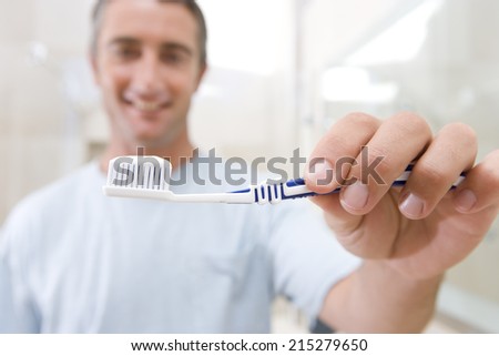 Man holding up toothbrush, smiling, portrait (focus on toothbrush)