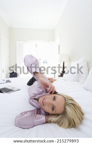Mature businesswoman lying on bed using mobile phone, smiling, portrait, elevated view